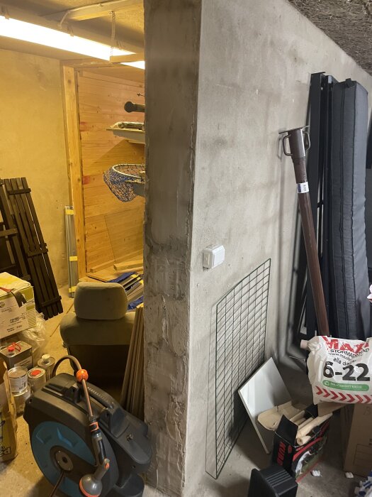 Öppning i betongvägg med verktyg och byggmaterial, inklusive en vattenslangvinda, ställningar och förvaringslådor runt omkring.
