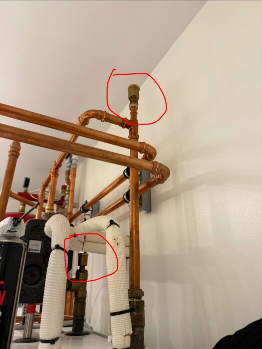 Kopparrör med ventiler i ett rörsystem markerade med röda cirklar, monterade på vit vägg. Några rör är isolerade.