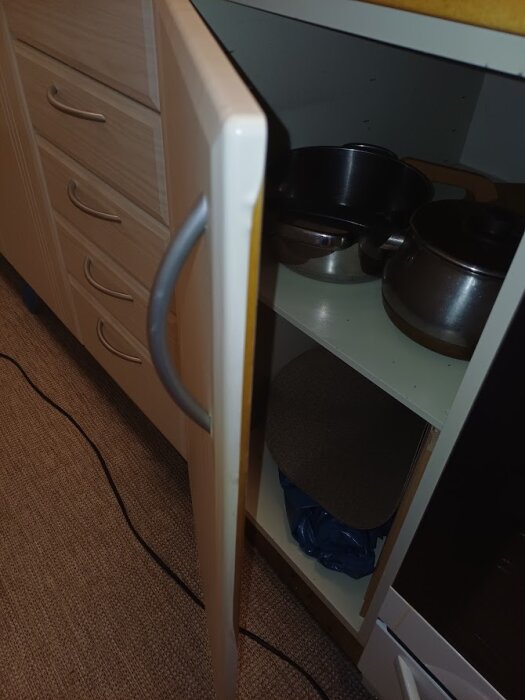 Öppet köksskåp med metallhandtag, exponerar kastruller och stekpannor inuti. Luckorna har foliebelagd yta.