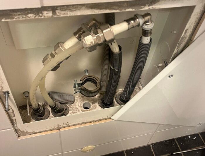 Fyra rör bakom en panel i ett badrum, potentiellt förberedda för vattenburen golvvärmeinstallation. Två rör anslutna, två oanslutna.