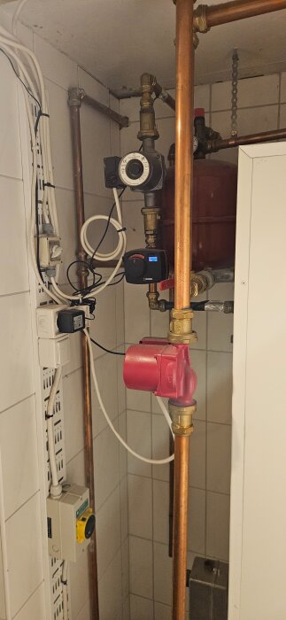 Värmesystem med rör och värmepump i källare, kopplingar och ledningar synliga nära expansionskärl.