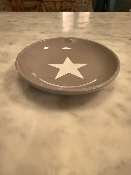 Grå keramikskål med vit stjärna på insidan, placerad på ett marmorbord.