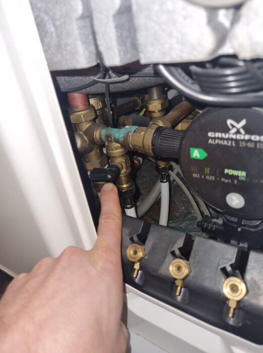 En hand pekar på en fastrostad ventil på en NIBE F750 värmepump. Ventilen är svår att vrida på grund av hårt vatten och brist på underhåll.