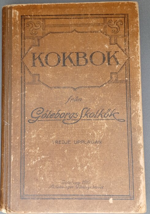 Äldre kokbok från Göteborgs skolköks tredje upplaga, utgiven 1916 med slitet brunt omslag och dekorativa detaljer.