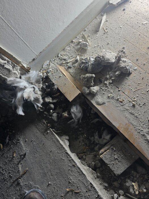 Bilden visar en del av ett golv under renovering med exponerad glasfiberisolering, träreglar och byggrester på betongbjälklag.