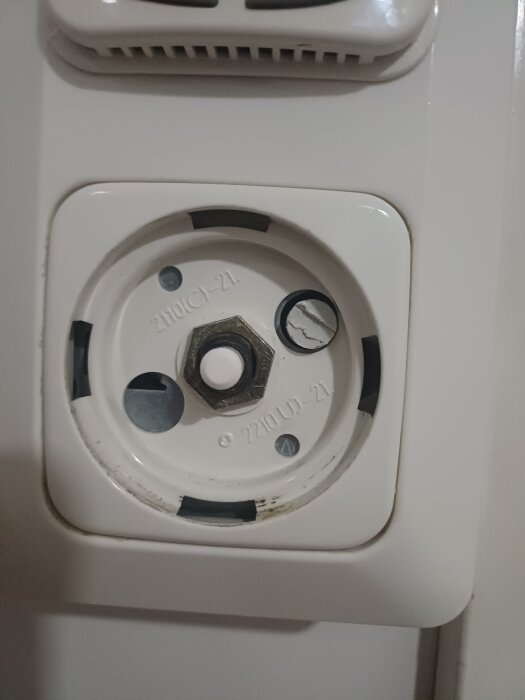Vit väggkontakt med skyddskåpa av och synliga skruvar, märkt med "2110 C1-21" och "2210 U1-21".