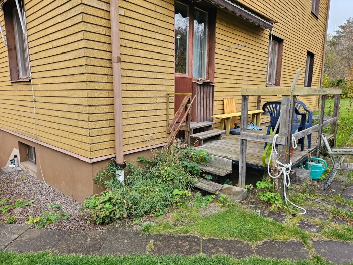 Gul fasad av klinkerplattor på ett mindre hyreshus, trätrall med stolar syns bredvid.