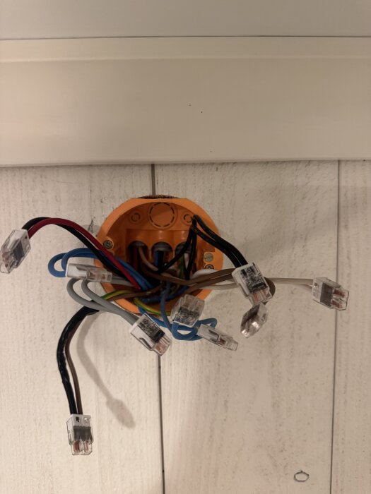 Elektriska kopplingar och kablar i en orange dosa ovanför en dörröppning mot en ljus träpanel.