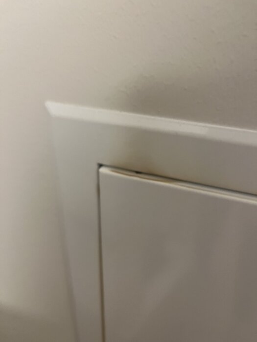 Vit fördelarskåp med gulnade fläckar i ett nybyggt radhusområde. Fläckarna sträcker sig upp på väggen. Mässingen på skåpet är mörk.