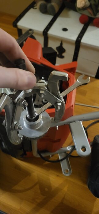 Närbild på en hand som håller ett verktyg, en avdragare, fäst vid en axel med en mutter och skiftnyckel, del av ett mekaniskt arbete.