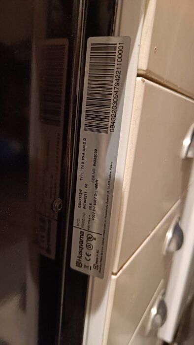 Etikett med modell- och serienummer på en Husqvarna-spis, modell QSG7132W, med information om tekniska specifikationer och certifieringar.