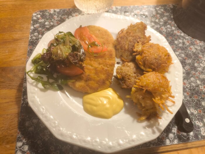 Schnitzel serverad med hashbrowns, sallad och mangoraja på en tallrik.