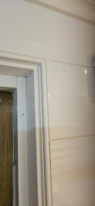 Fönsterkarm i badrum med kakel på väggen, delvis synlig, med detaljerad fokus på karmen och omgivande kakelplattor.