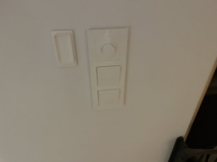 Vägg med strömbrytare och dimmer i vitt intill en dörröppning och ett handtag synligt i hörnet.