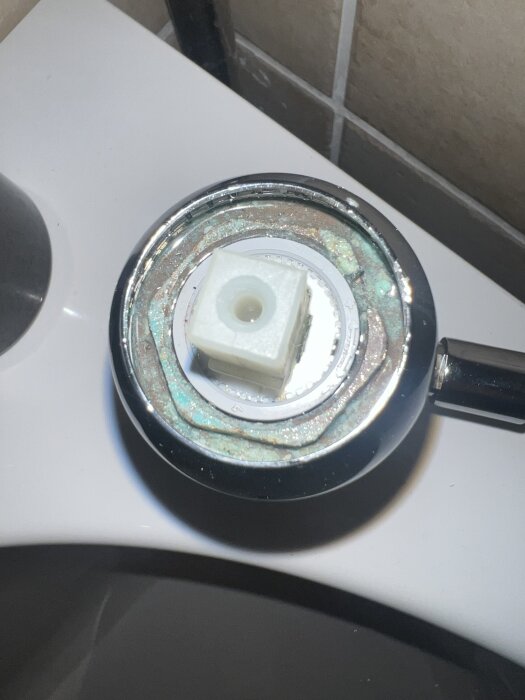 Övre delen av en blandare med avlägsnad hylsa visar invändig komponent och mutter, på en vit diskbänk.