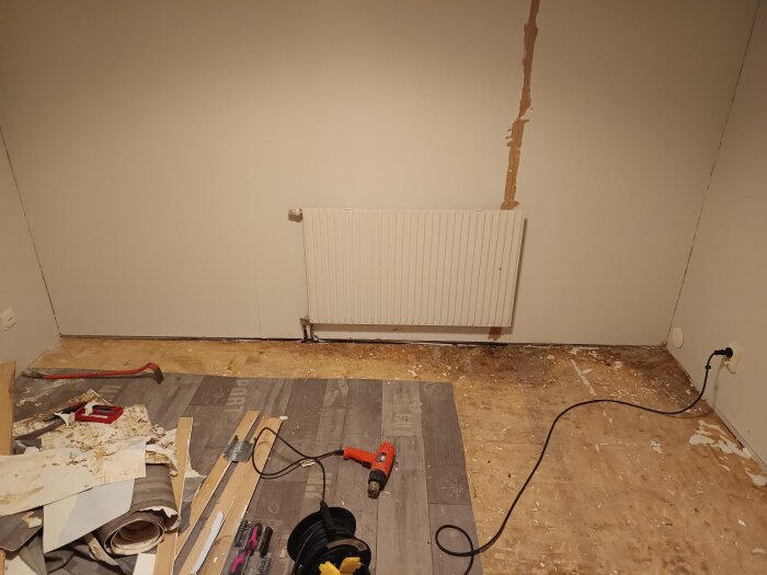 Renovering av rum i suterränghus från 1978. Golv delvis upptaget med synlig spånskiva, verktyg på golvet, trasig väggfärg och synligt golvlister.