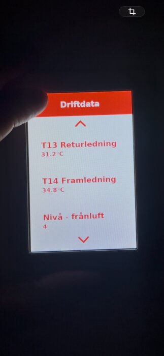 Hand håller skärm med Thermia Ventec driftdatadisplay: T13 Returledning 31.2°C, T14 Framledning 34.8°C, Nivå - frånluft 4.