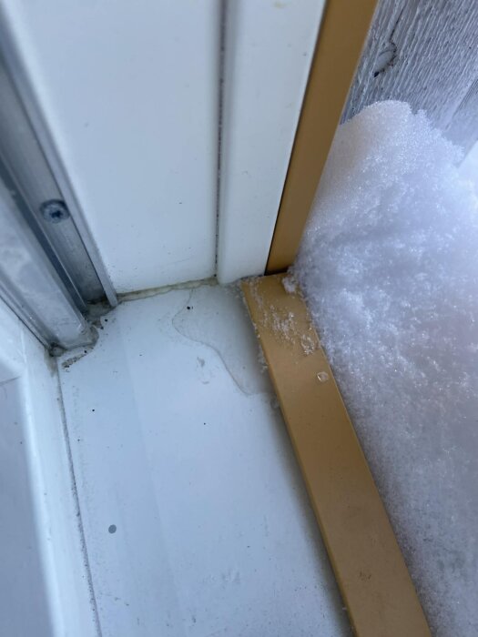 Kondens och isbildning syns på fönstrets insida och bottenkarm, med snö utanför.
