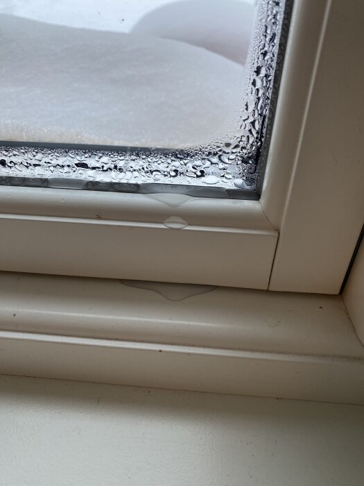 Kondens vid nederkanten av ett fönster, med isbrytna droppar och frost synligt på fönsterrutan.