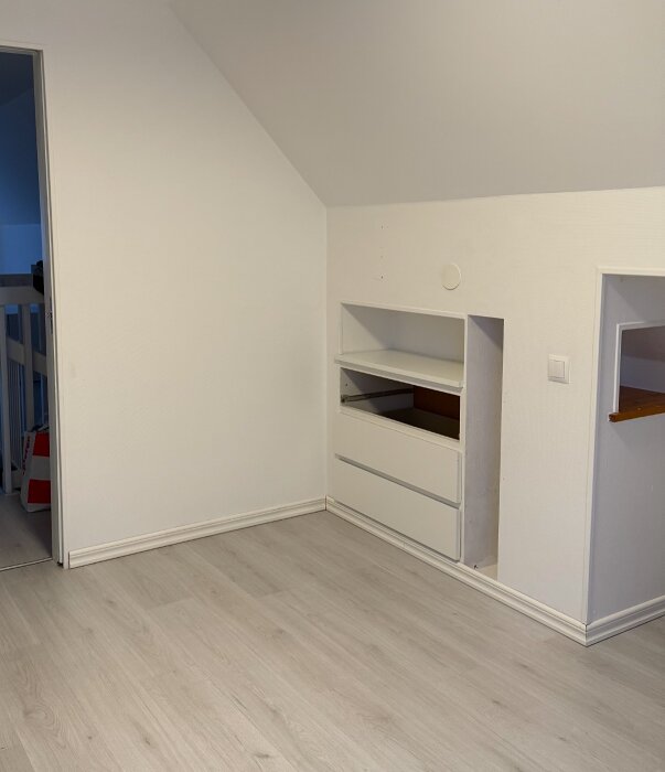 Inre hörn av rum med delvis riven platsbyggd byrå, intill trappa, och synligt golv utan isoleringsmaterial.