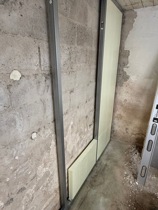 Vägg med betongblock och metallramar, delvis täckt med isoleringsskivor. Byggmiljö, ofärdigt renoveringsprojekt.