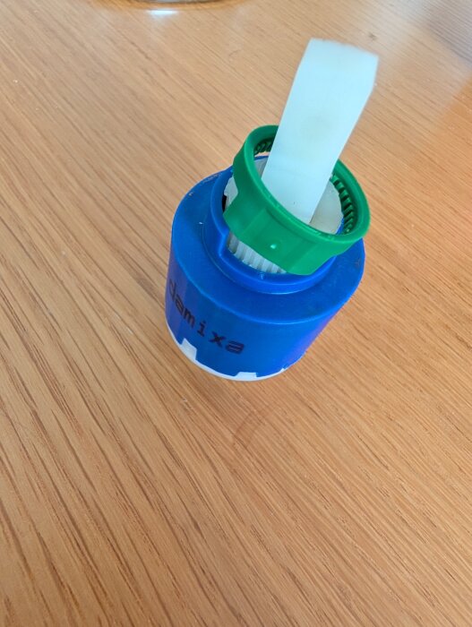 Blå och vit plastdel med en lös grön ring, placerad på ett träbord.