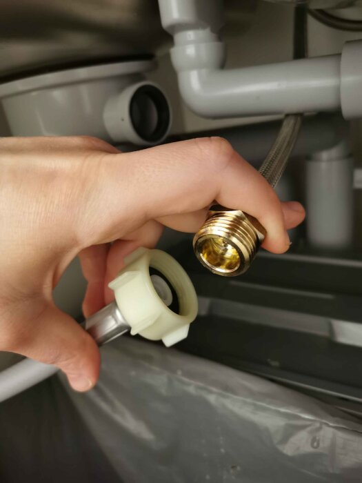 Hand håller upp en inloppsslang och en mässingskoppling under diskbänken, där kopplingen inte passar slangen.