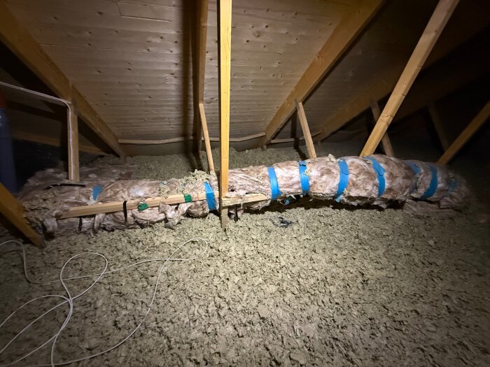 Vattenrör på vinden, isolerade med material och blå remmar, kan ses mellan bjälkar i taket. Eventuell orsak till problem med vattentillförsel.