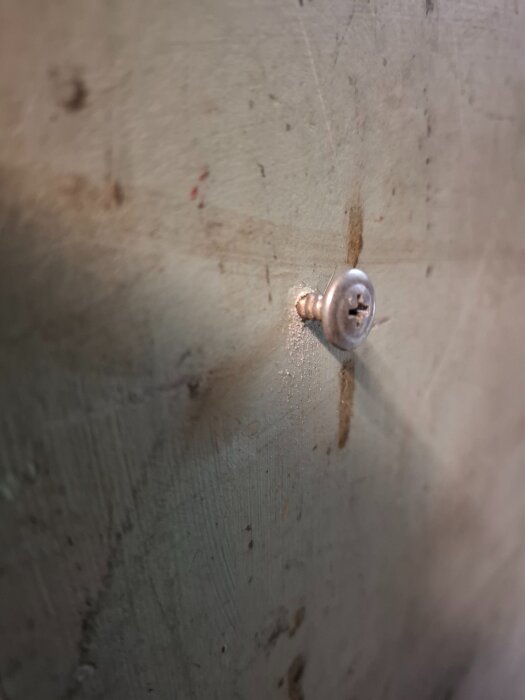 Närbild på en självborrande skruv delvis inskruvad i en sliten yta, troligen eternit, med spår av tidigare försök med en annan skruv.