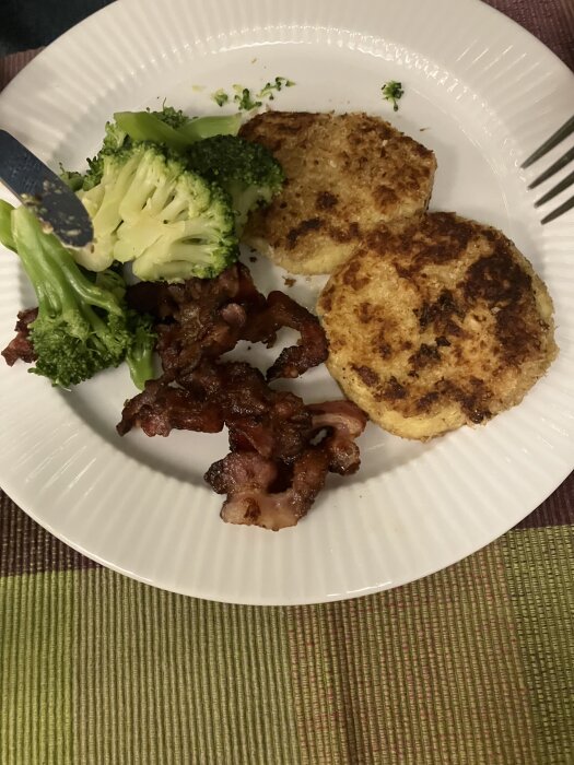 Tallrik med potatisbullar, bacon och broccoli, serverad på en vit tallrik.