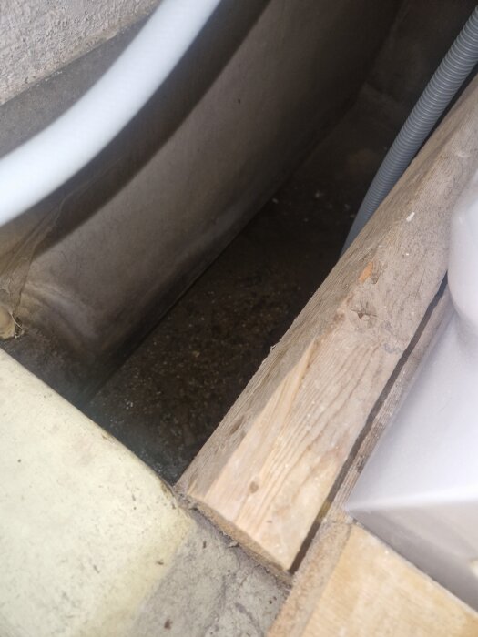 Betongfundament i tvättstuga med primitivt spillvattenutrymme och synlig fuktskada där vatten från avloppsslang hamnat direkt på golvet.