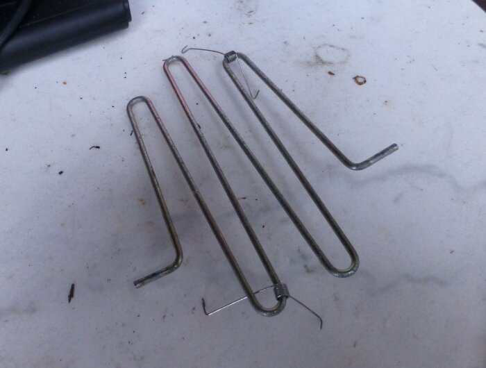 Metallgaller och två fjädrar på ett bord, delar av en Stiga Snow Breeze snöslunga.