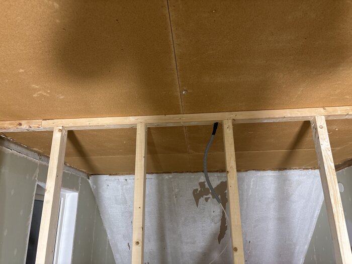 Vägg under konstruktion med träreglar och kabelrör, oisolerat tak och väggar i byggprocess.