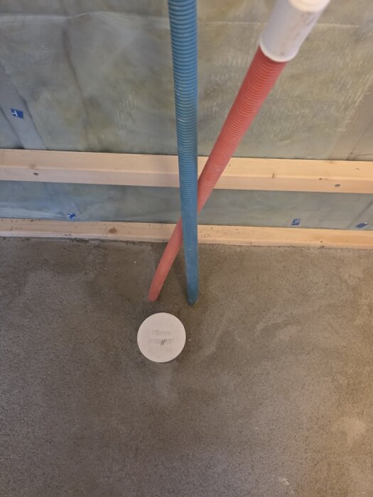 Rör i blå och röd färg som kommer upp ur en betongplatta, med en cirkulär plugg märkt "75mm integr.s." bredvid.