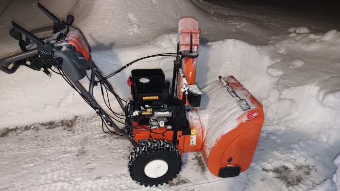 Ny orange snöslunga står på en snötäckt yta, redo för vinterbruk.