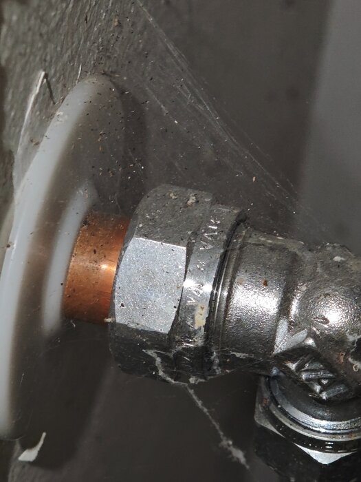 Närbild av ett smutsigt rör i ett hörn, med spindelväv och damm på metallbeslagen.