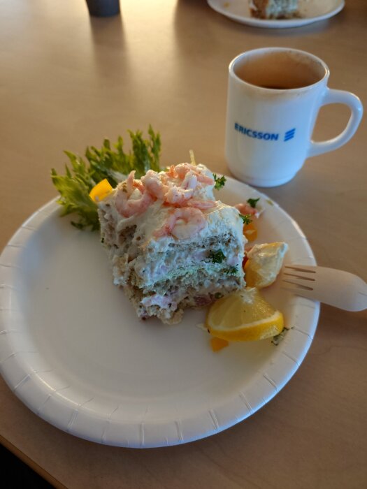 Räksmörgåstårta på papperstallrik med citronklyfta och sallad bredvid en kopp kaffe.