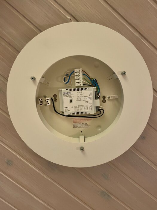 Vit plafond från Atelje Lyktan med synlig styr- och reglerenhet, kablar och monteringsdetaljer på en träfärgad takpanel.