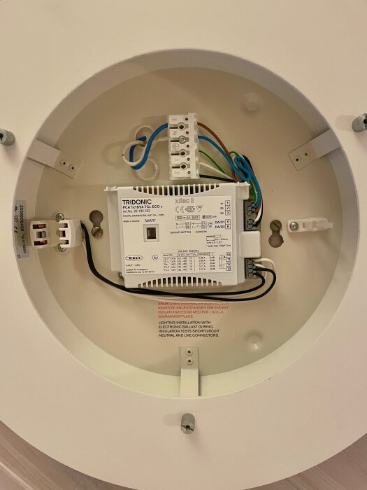 Elektronisk drivdon installerat i plafondlampans armatur, med flera anslutna kablar och texten "Tridonic PCA 1x18/24 TCL ECO C".