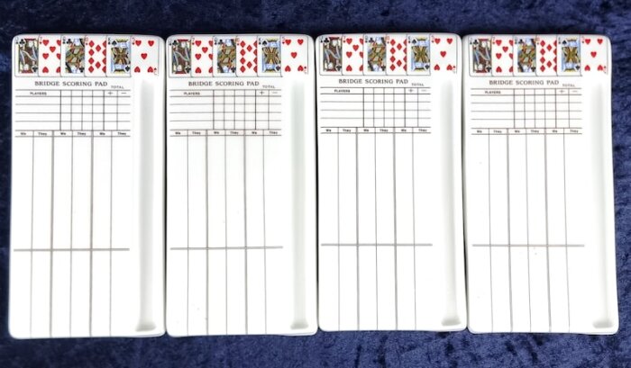 Fyra bridgeblock för poängräkning med kortmotiv högst upp och rutnät för notering av spelarpoäng, svart text på vit bakgrund.