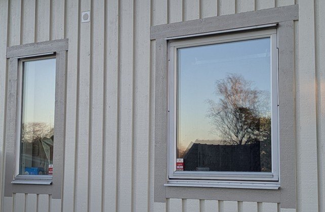 Fasad med två fönster, reflektion av omgivande natur i glaset, fokus på över/droppblecken ovan och under fönstren.