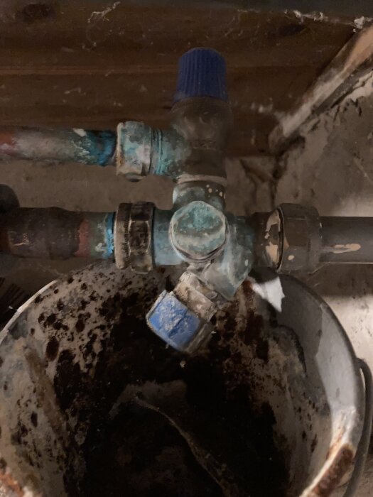 Kopparrör under diskbänk med blå ventil, pajärnkrukor och korroderade kopplingar, varmvattenledning från pannan fortsätter till kranen och avloppet.