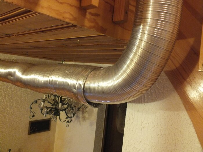 Korrugerad aluminiumrör som hänger i taket i en gillestuga, nära träpaneler; del av värmespridningslösning.