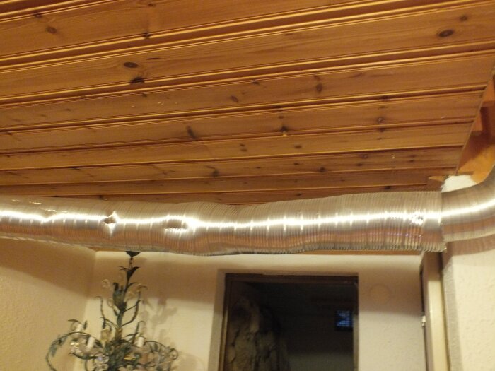 Korrugerat aluminiumrör hänger under trätak i en källare för att leda värme från en kamin till övervåningen.