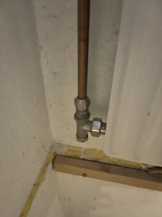 Radiatorrör i hörnet av en källarvägg. Röret har en koppling ovanför golvlisten och ansluter till radiatorn.