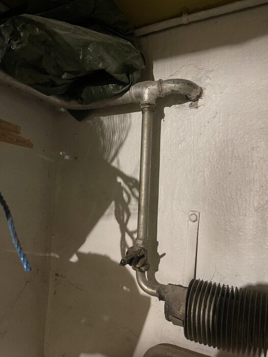 Röranslutning med ventil och packning i en källare, synlig luftningsventil och böjd sektion med grönt material ovanstående.