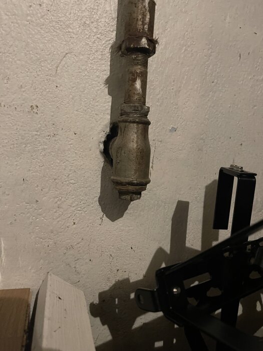 Gammalt rör mot en vit vägg i en källare, med närbild på en rörkoppling och omgivande utrustning, del av diskussion om radiatorproblem.