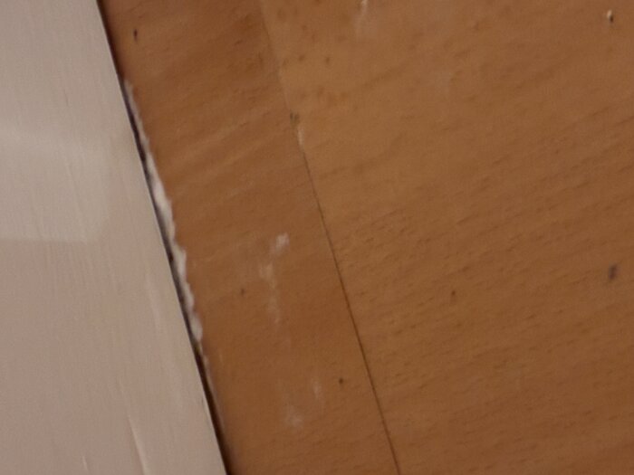 Fog mellan vit vägg och träpanel, synlig kitt eller silikon som delvis har runnit.