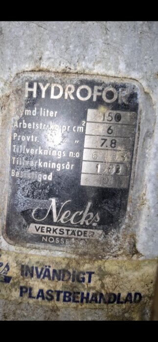 Skylt på hydrofortank med teknisk information: kapacitet 150 liter, tryck 6 kg/cm², provtryck 7,8. Tillverkad av Necks Verkstäder, 1983.