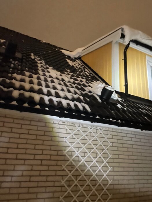 Takfot på ett hus täckt med snö, betongpannor och en nyligen installerad takhuv syns. Snön har rasat ner, potentiellt skador från detta.